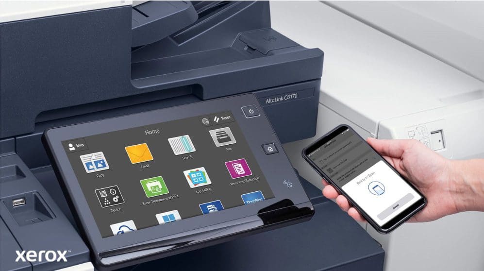 Gros plan de la main d'une personne tenant un smartphone, qui est connecté sans fil au panneau de commande à écran tactile d'une imprimante multifonction Xerox, mettant en valeur les capacités d'impression et de numérisation mobiles transparentes de Xerox ConnectKey.