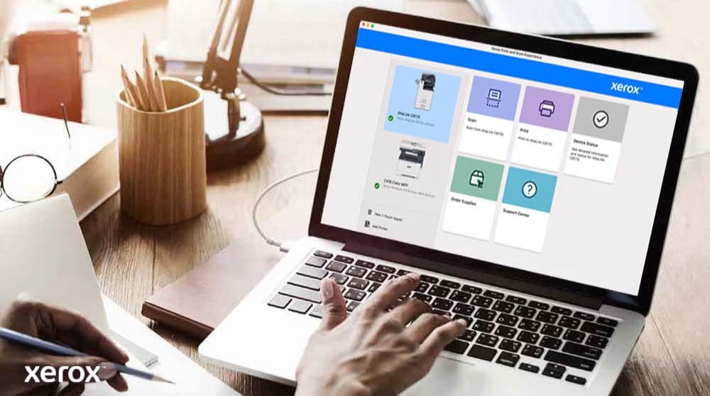 Les mains d'une personne sont posées sur un clavier d'ordinateur portable et l'écran affiche l'interface Xerox Print and Scan Experience avec des options telles que Numériser, Imprimer, État de l'appareil, Commander des fournitures et Centre d'assistance, indiquant un contrôle convivial.