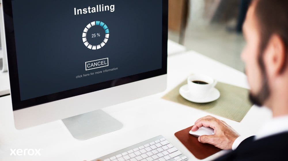 Vue rapprochée d'un écran d'ordinateur affichant une barre de progression « Installation » à 25 %, avec la main d'une personne sur une souris d'ordinateur à côté d'une tasse à café, illustrant une configuration logicielle facile.