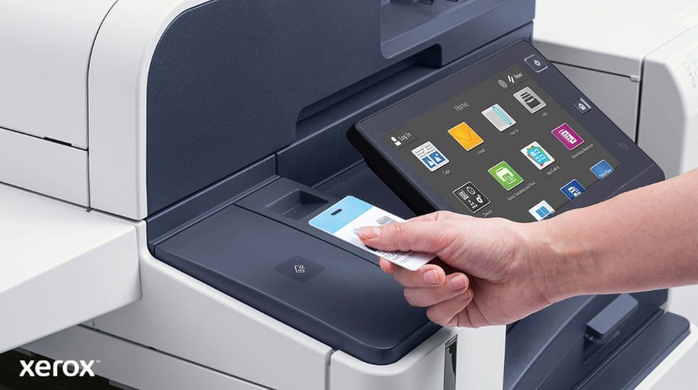 Une main tient une carte de sécurité et la scanne près du lecteur de carte d'une imprimante multifonction Xerox moderne dotée d'un grand écran tactile affichant diverses icônes d'application.